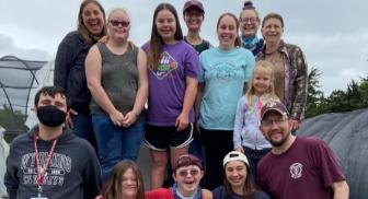 Group of people smiling in an outdoor setting, some wearing colorful shirts and caps.