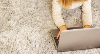 Person lying on carpet typing on a laptop.