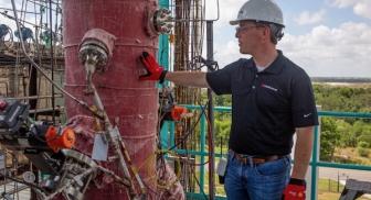 Engineer inspecting industrial pipe outdoors, wearing hard hat and gloves.