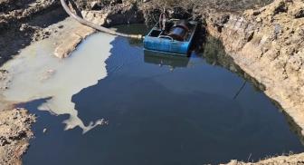 A large muddy pit with a blue container partially submerged.