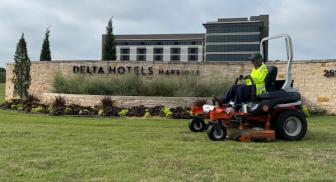 Worker mowing grass in front of Delta Hotels building.