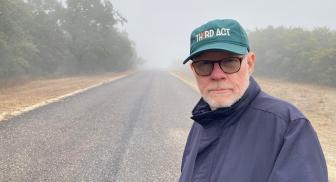 Man in a jacket and cap standing on a foggy road.