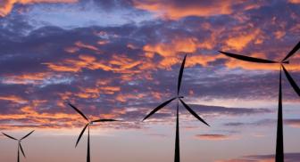 Wind turbines against a vibrant sunset sky with colorful clouds.