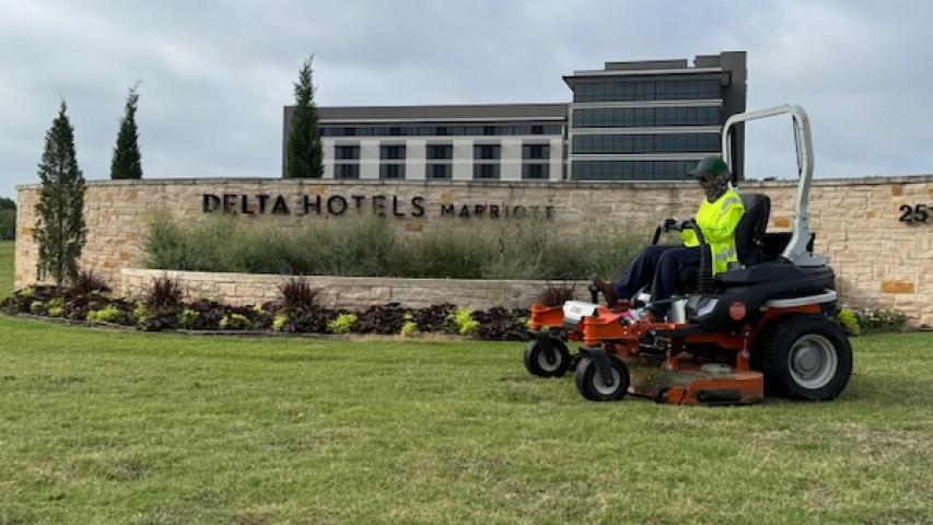 Worker mowing grass in front of Delta Hotels building.