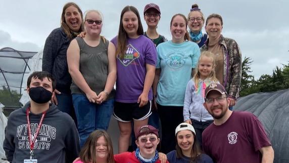 Group of people smiling in an outdoor setting, some wearing colorful shirts and caps.