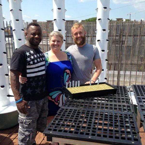 Three people smiling on a rooftop with gardening tables and planters.