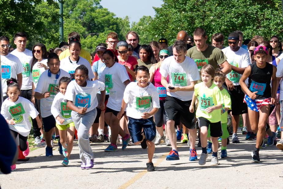 Kids and adults running in a group, wearing race bibs and colorful shirts.
