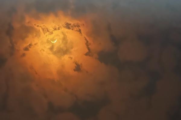 Crescent moon glowing through thick orange clouds.