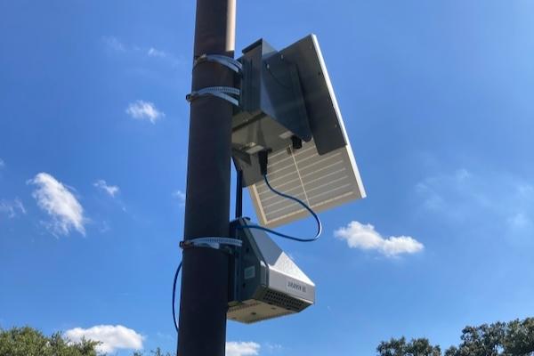 Solar panel and air monitoring devices mounted on a pole under a clear blue sky.