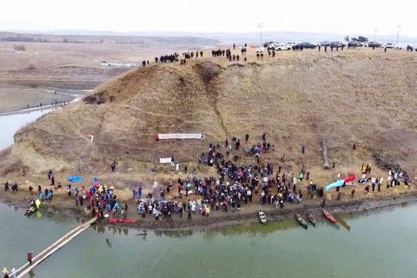 Crowd gathered on a hill by a river, aerial view.