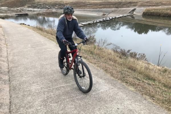 Cyclist riding along a riverside path in casual gear.