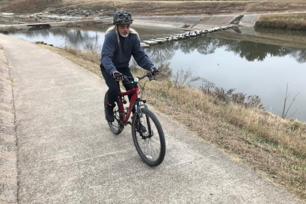 Cyclist riding on a pathway beside a river on an overcast day.