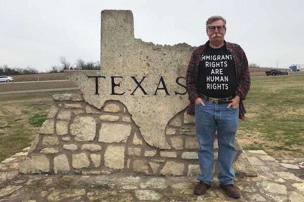 Man standing next to a stone Texas sign in a grassy area.
