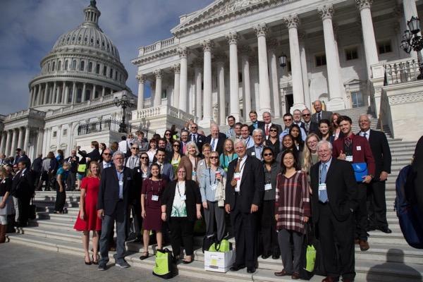 Group of people gathered on Capitol steps, clear day, building in background.