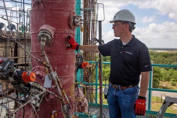 Engineer inspecting industrial pipe outdoors, wearing hard hat and gloves.