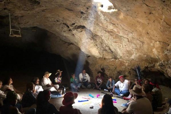 Group of people sitting in a circle inside a dimly lit cave.