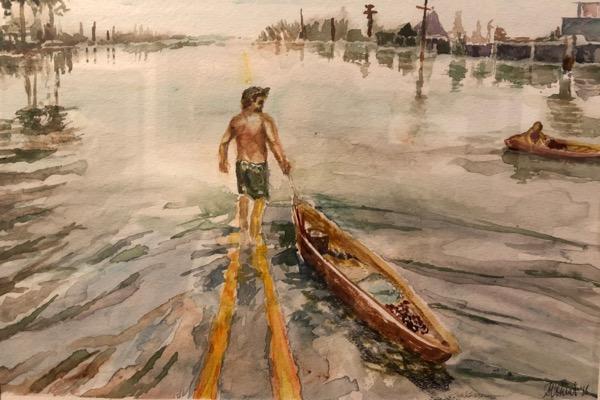 Man in shorts pulling a canoe on a flooded street; palm trees in the background.
