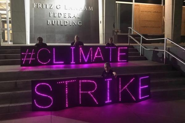 Protesters holding illuminated signs reading "#Climate Strike" on building steps at night.