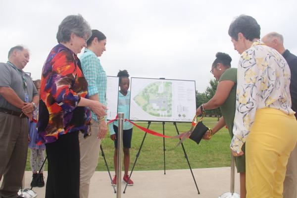 Group of people at a ribbon-cutting ceremony outdoors, with a map on display.