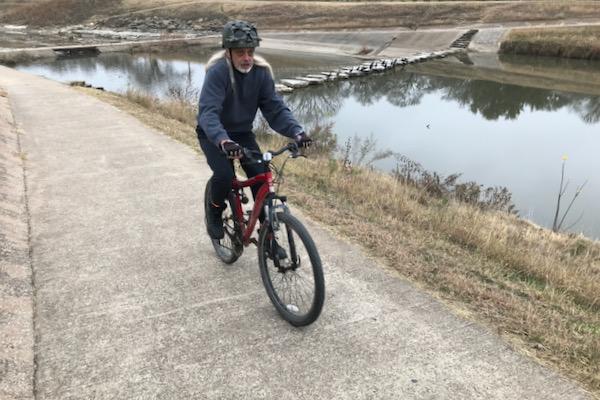 Cyclist riding along a riverside path on a cloudy day.