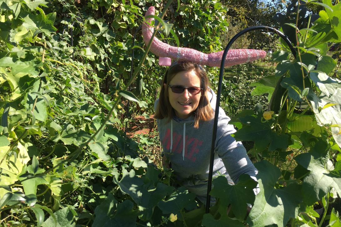Woman in sunglasses surrounded by green foliage, smiling in a garden.