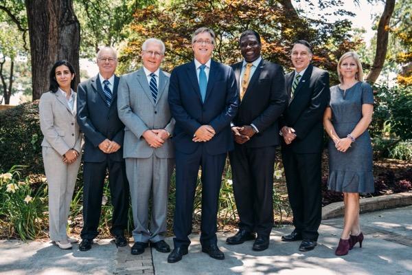 Seven people in formal attire standing outdoors, smiling.