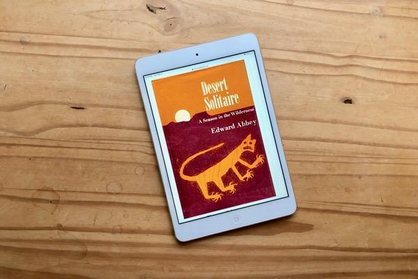 E-reader on wooden table displaying a desert-themed book cover.