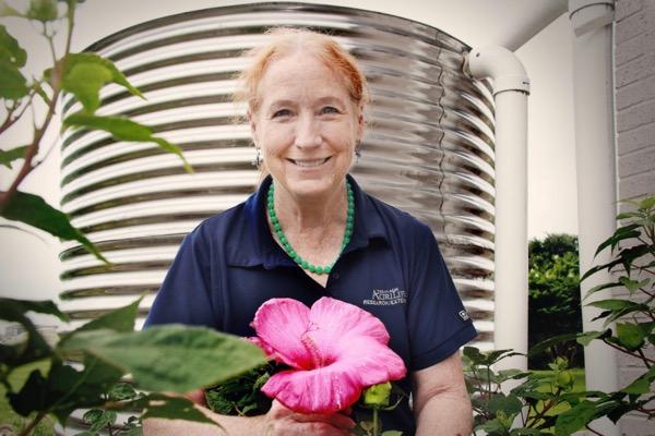 Woman smiling, holding a large pink flower, with a water tank in the background.