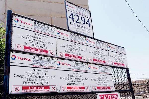 Metal sign displays oil well information and addresses against a clear sky.