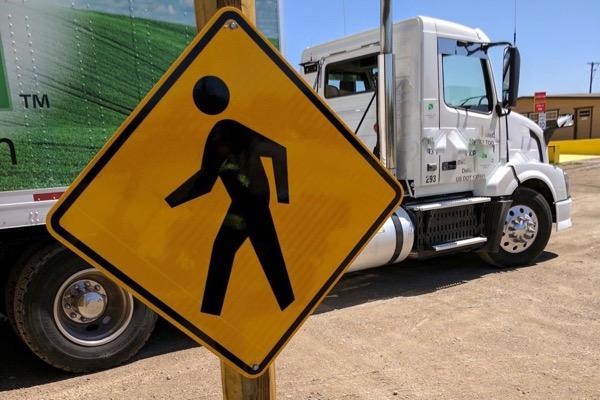 Yellow pedestrian crossing sign near a white truck.