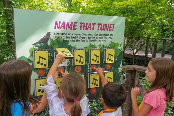 Children pointing at a musical note display in an outdoor setting.