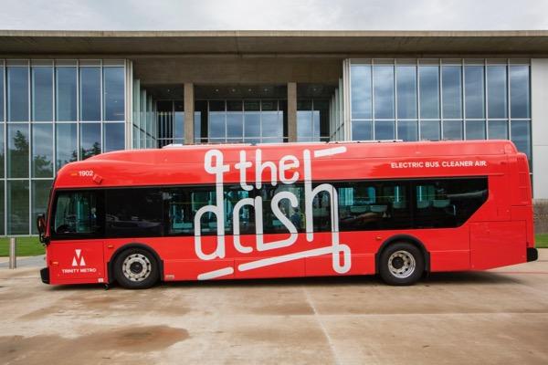 Red electric bus with "the dash" text, parked outside a modern glass building.