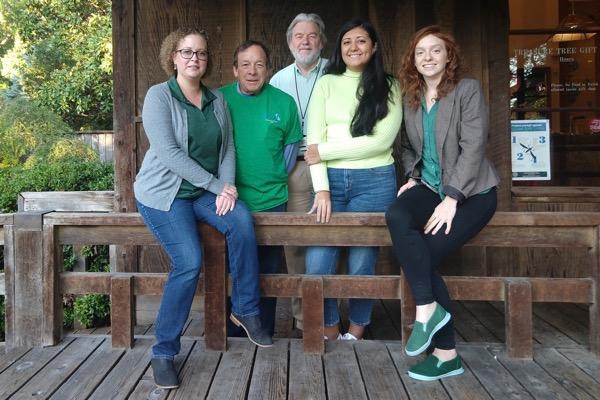 Five people sitting on a wooden bench, smiling at the camera.