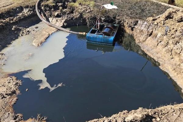 A large muddy pit with a blue container partially submerged.