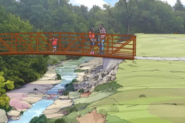 Red footbridge over a stream with people, surrounded by greenery.