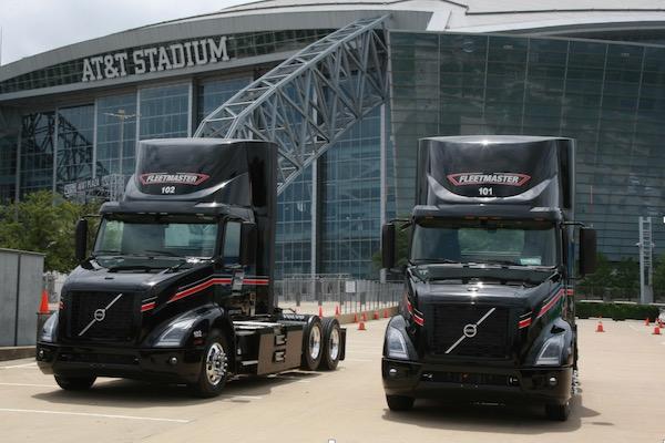 Two black trucks parked outside a large stadium.