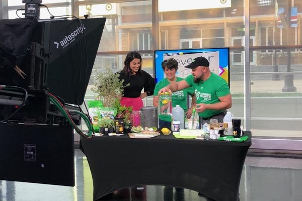 TV studio scene with three people at a table, preparing food.
