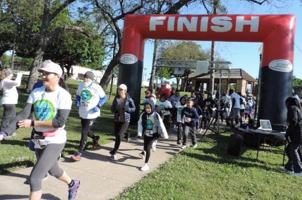 Runners crossing a finish line in a park.