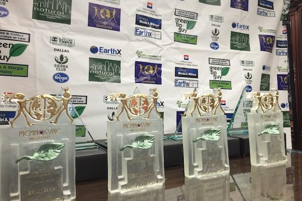 Four trophies with gold tops on a table, backdrop with logos.