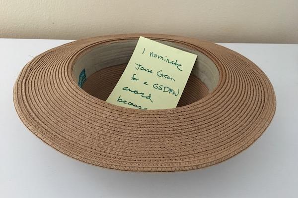 Brown straw hat on a white surface with a yellow note inside.