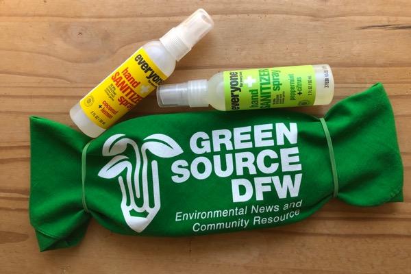 Green pouch with logo, two small spray bottles on wooden surface.