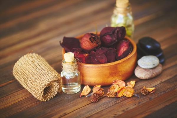 Potpourri in a wooden bowl, oils, stones, and a woven mat on a wooden surface.