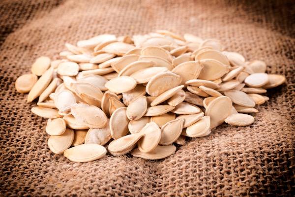 Pumpkin seeds scattered on burlap fabric.