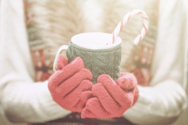 Cozy mug with candy cane, held with pink gloves.