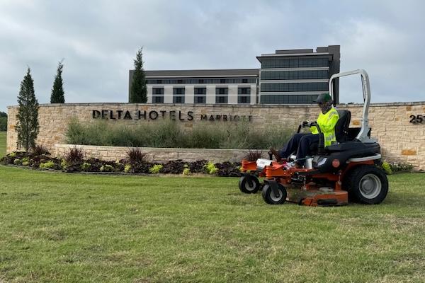 Worker mowing grass in front of Delta Hotels building.