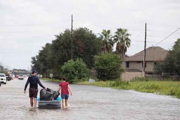 Two people pull a raft in a flooded suburban street.
