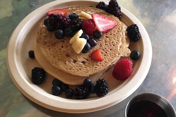 Pancakes topped with sliced bananas, strawberries, and mixed berries on a plate.
