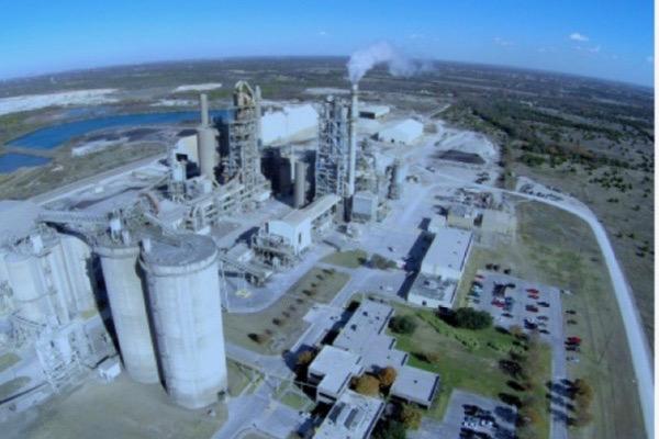 Aerial view of an industrial plant with smoke, surrounded by fields.