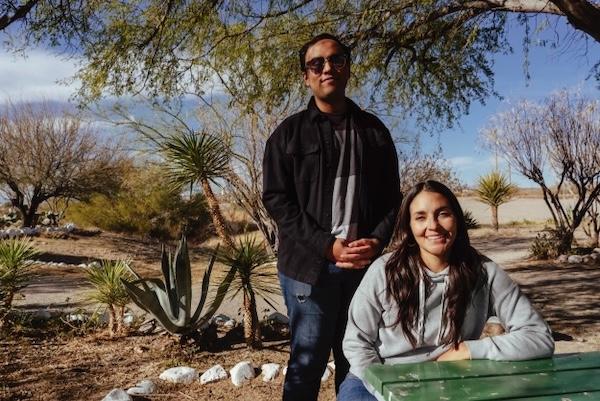Man and woman outdoors, smiling near trees and desert plants.
