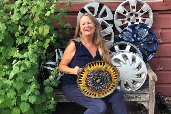 Smiling woman on bench with colorful wheel covers, green plants nearby.